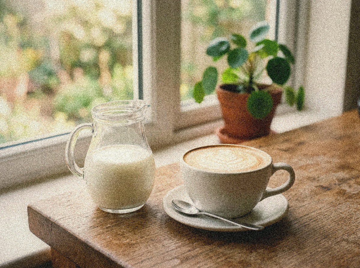 KI-generierter Lifestyle-Render Milchkännchen neben Cappuccino mit Latte-Art. Markenneutral; keine Maschinendarstellung.